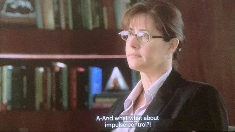 Dr. Melfi is sitting in her office with her hair up and glasses on talking to Tony.